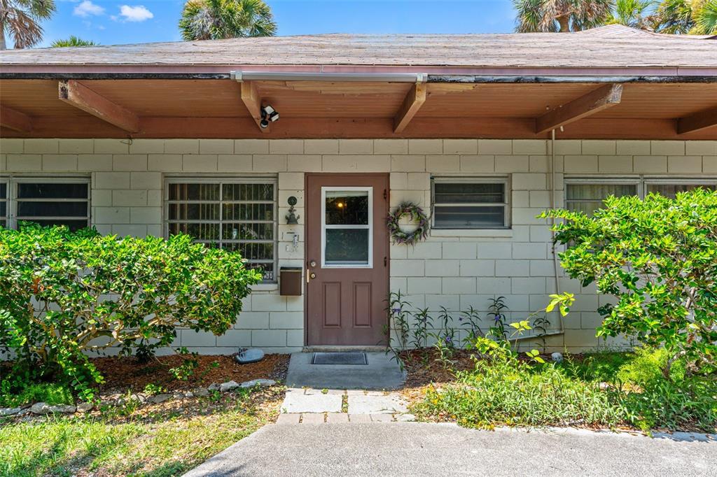 The exterior of a single-story home features a brown door, concrete block walls, and landscaping — 1230 S ORLANDO AVENUE, COCOA BEACH, FL
