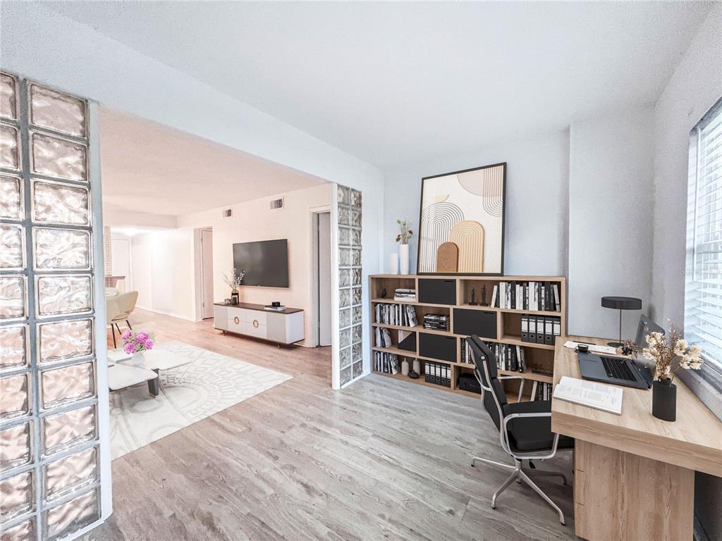 A home office with wood-look flooring and a bookshelf opens into a living area — 4204 HERON WAY UNIT B304, BRADENTON, FL