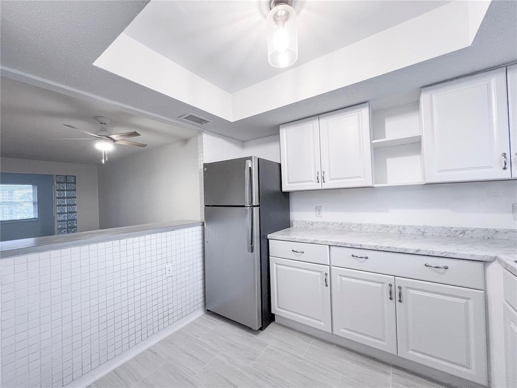A kitchen features white cabinets, a stainless steel refrigerator, and a white tiled half wall — 4204 HERON WAY UNIT B304, BRADENTON, FL