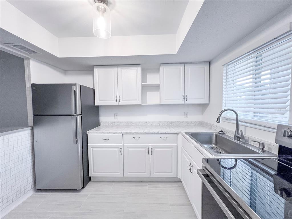 A kitchen features white cabinets, marble-look countertops, stainless steel appliances, and light-colored tile flooring — 4204 HERON WAY UNIT B304, BRADENTON, FL