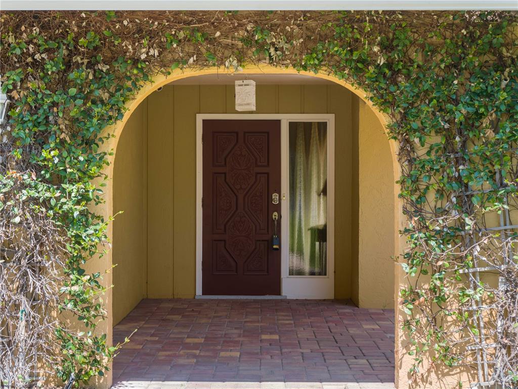 A front entryway features a dark wood door with glass sidelight under a vine-covered arch — 424 BAYCREST DRIVE, VENICE, FL