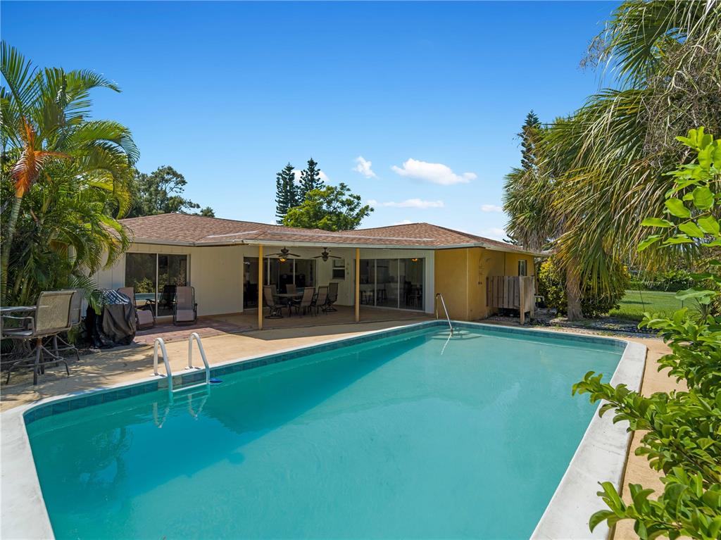 A backyard swimming pool sits in front of a house with a covered patio — 424 BAYCREST DRIVE, VENICE, FL