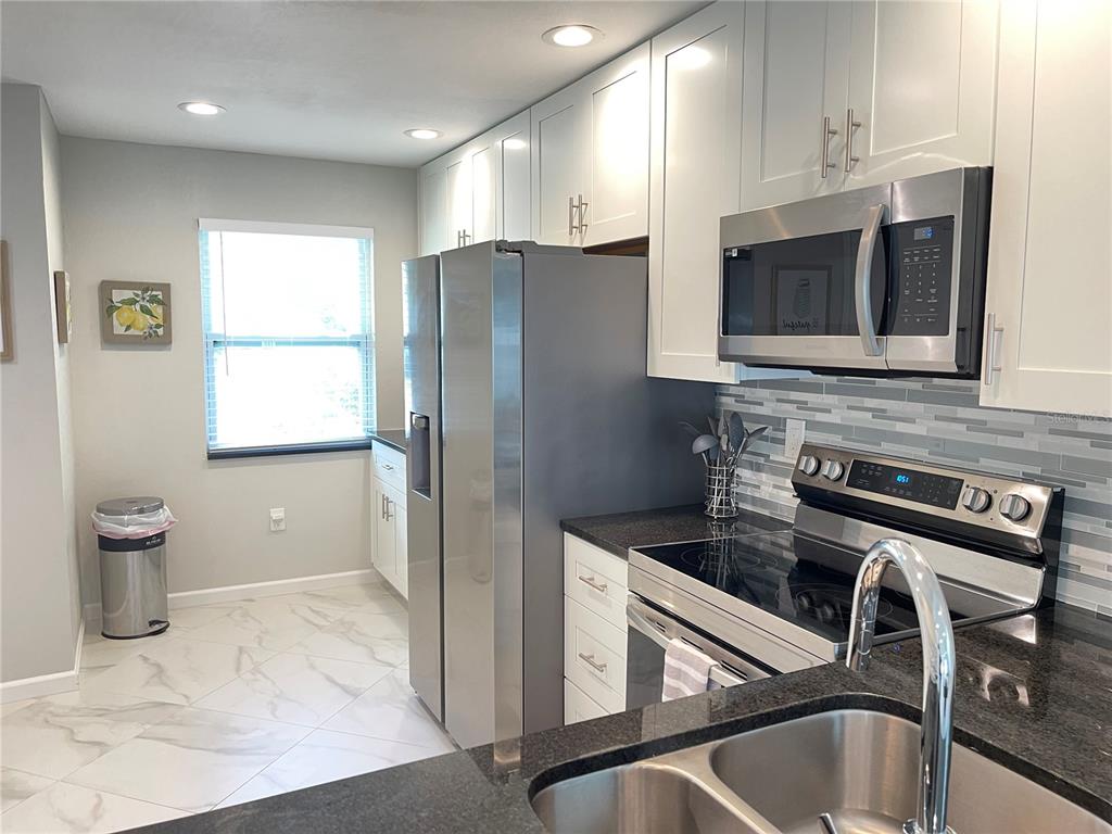 A kitchen features white cabinets, stainless steel appliances, dark countertops, and light-colored tile flooring — 1821 ORANGE BOULEVARD WAY, PALM HARBOR, FL