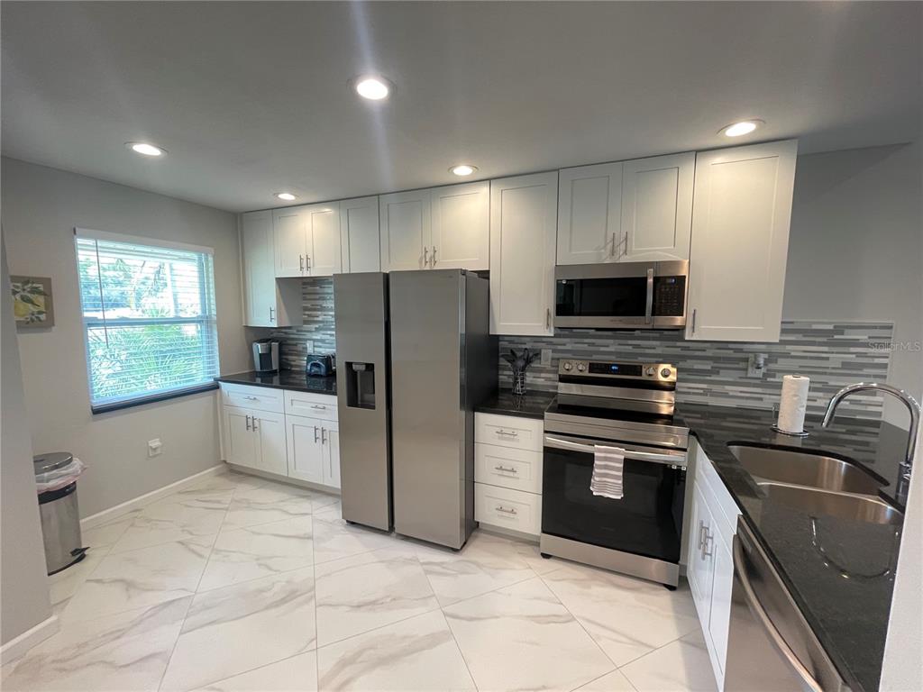 A kitchen features white cabinets, stainless steel appliances, black countertops, and light-colored tile flooring — 1821 ORANGE BOULEVARD WAY, PALM HARBOR, FL