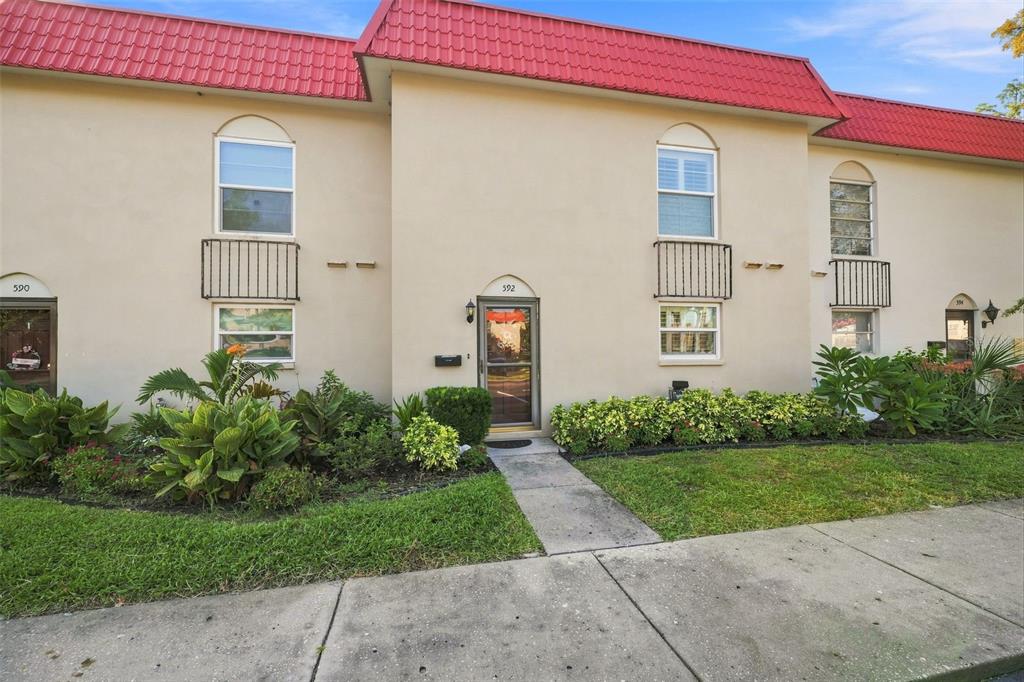 A two-story apartment building exterior features a red metal roof and beige stucco walls — 2700 BAYSHORE BOULEVARD UNIT 592, DUNEDIN, FL