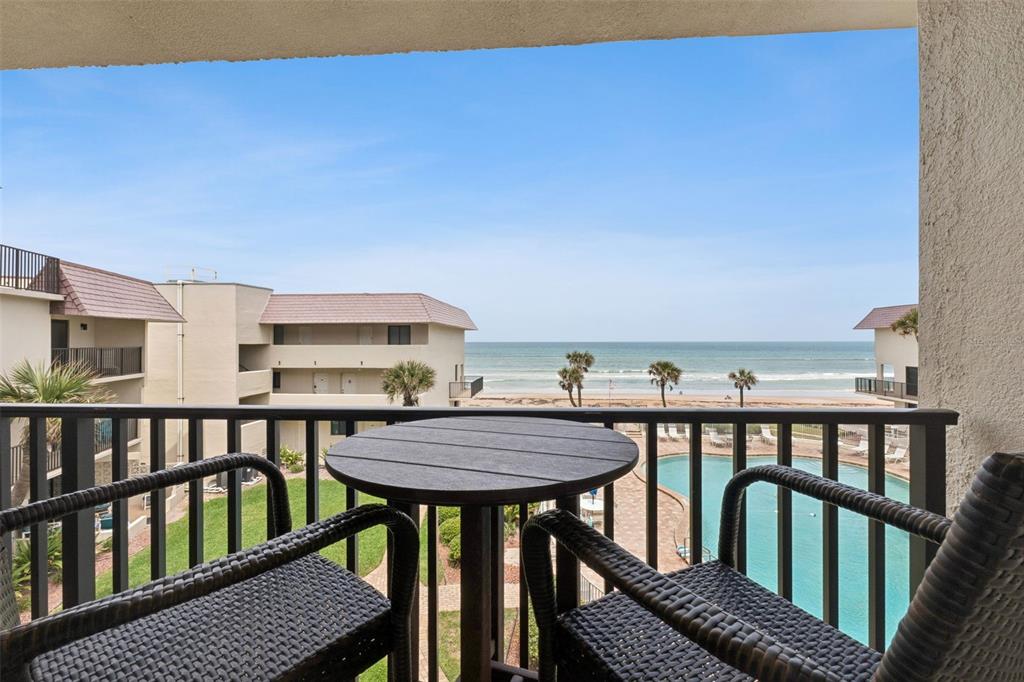 A balcony with a small table and chairs overlooks a swimming pool and the ocean — 935 OCEAN SHORE BOULEVARD UNIT 3020, ORMOND BEACH, FL