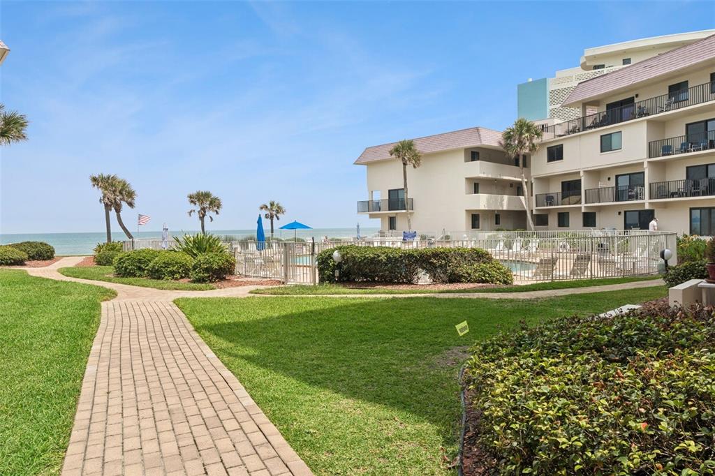 A paved walkway leads toward a swimming pool area beside a multi-story beachside building — 935 OCEAN SHORE BOULEVARD UNIT 3020, ORMOND BEACH, FL