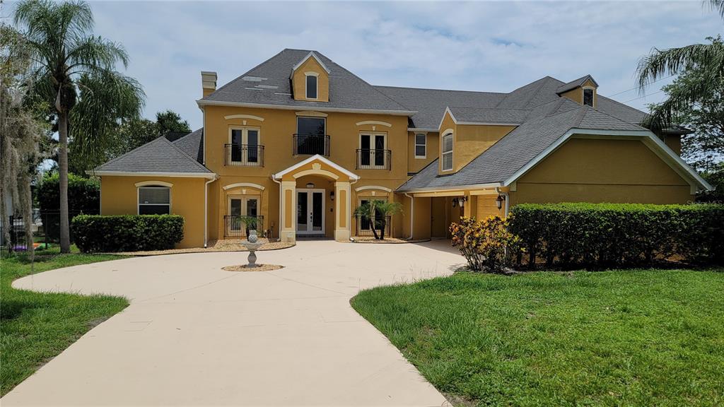 A two-story yellow house with a gray roof and a large concrete driveway — 13503 LAKE CAWOOD DRIVE, WINDERMERE, FL