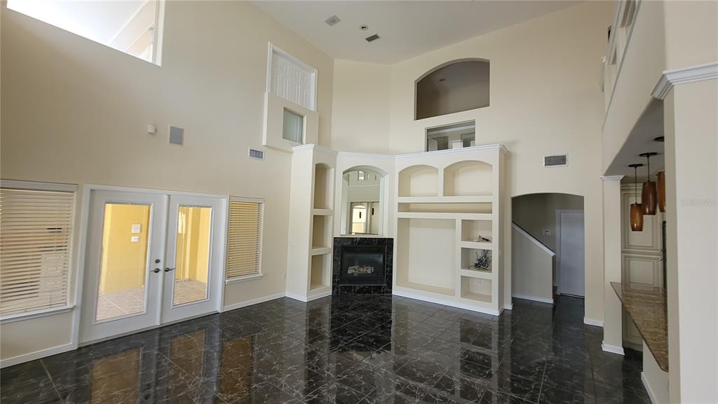 A high-ceilinged living room features dark marble flooring, a fireplace, and built-in shelving — 13503 LAKE CAWOOD DRIVE, WINDERMERE, FL