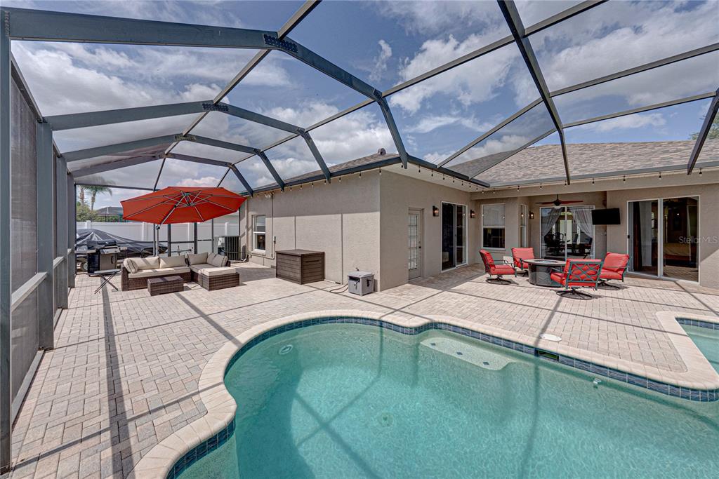 A screened-in patio features a swimming pool, outdoor seating, and a red umbrella — 1542 SWAMP ROSE LANE, TRINITY, FL