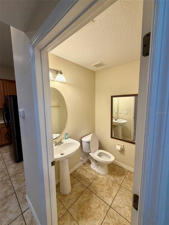 A small half bathroom features a pedestal sink, a toilet, and tan tile flooring — 6224 ZANE DRIVE, MOUNT DORA, FL
