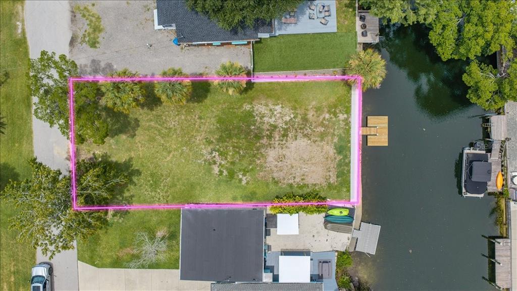 An aerial view shows a vacant grassy lot situated between two houses along a canal — 7250 COVENTRY COURT, WEEKI WACHEE, FL