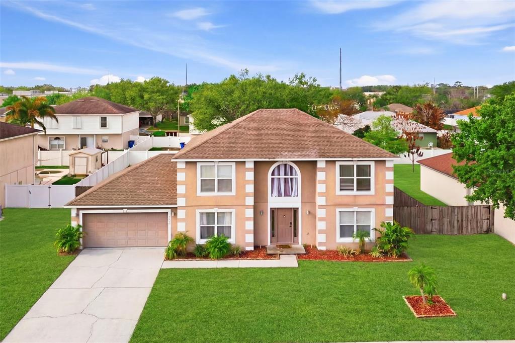 A two-story suburban house with a tan stucco exterior, white corner accents, and a garage — 1912 MAURY ROAD, ST CLOUD, FL