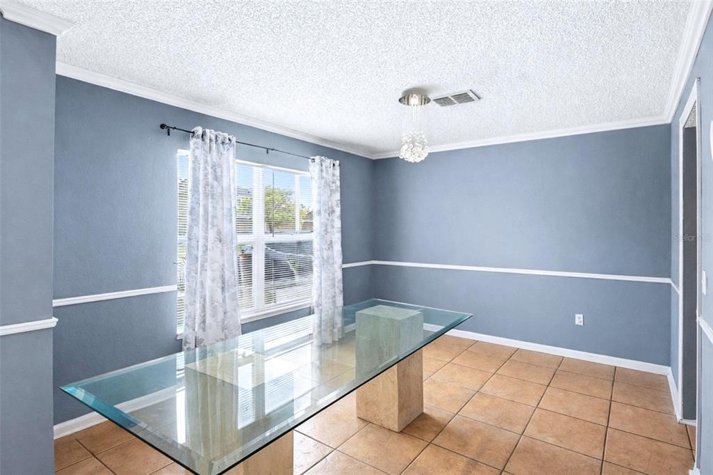 A dining room with blue walls, tile flooring, a glass table, and a crystal chandelier — 1912 MAURY ROAD, ST CLOUD, FL