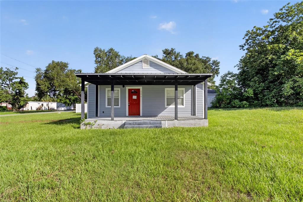 A light blue house with a red front door and a covered porch at sunset — 4104 ORANGE AVENUE SE, HIGHLAND CITY, FL