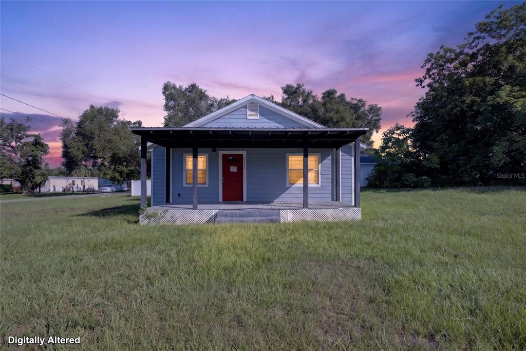 A light blue house with a red front door and a covered porch at sunset — 4104 ORANGE AVENUE SE, HIGHLAND CITY, FL