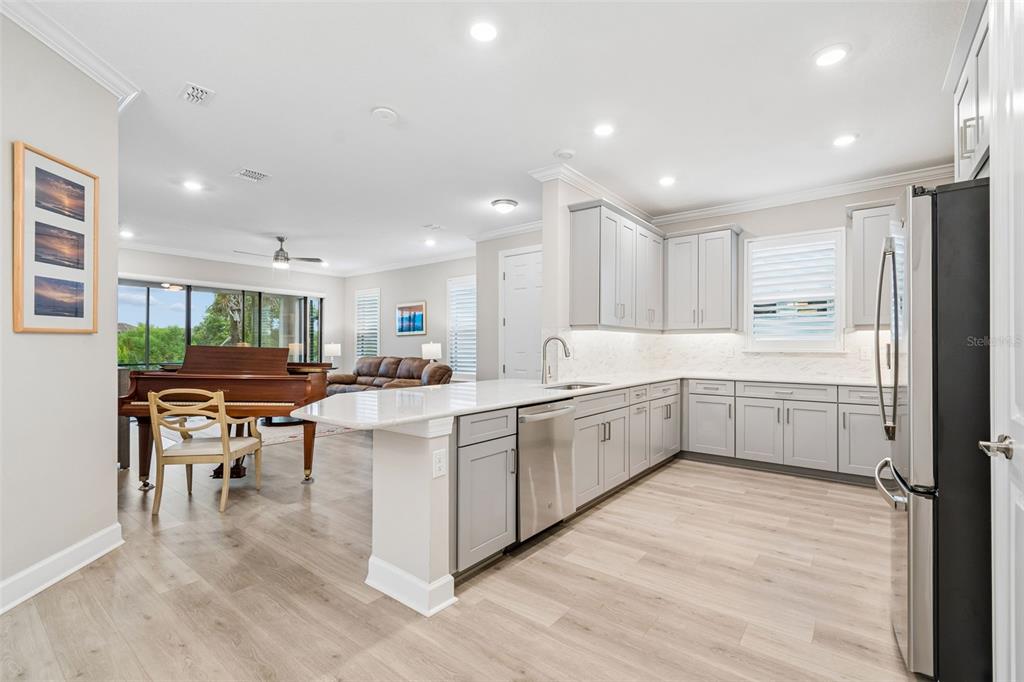 A modern kitchen with light gray cabinets and white countertops overlooks a living area with a piano — 4618 ROSATTI ROAD, WESLEY CHAPEL, FL