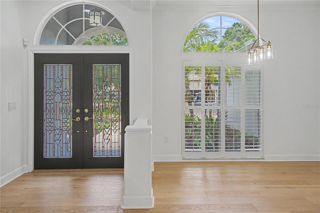 An entryway featuring a dark double door with decorative glass, arched windows, and hardwood flooring — 3692 JOHNATHON AVENUE, PALM HARBOR, FL