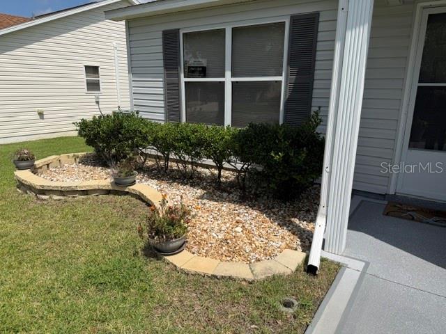 A landscaped garden bed with shrubs and potted plants sits in front of a house exterior — 1413 BLUEBERRY WAY, THE VILLAGES, FL