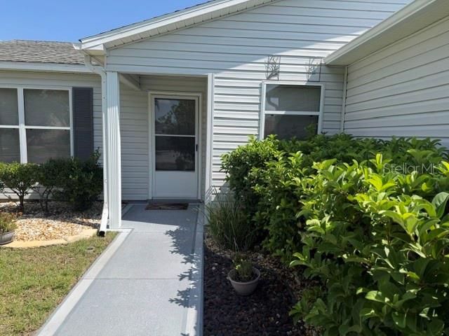 A white-sided house exterior features a front door, a concrete walkway, and green landscaping — 1413 BLUEBERRY WAY, THE VILLAGES, FL