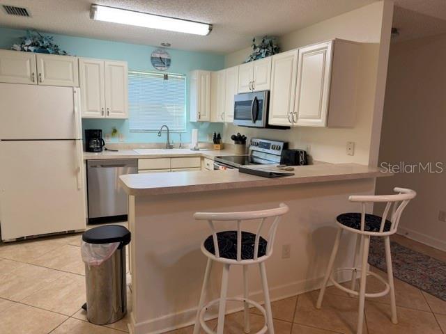 A kitchen features white cabinets, stainless steel appliances, a breakfast bar, and two bar stools — 1413 BLUEBERRY WAY, THE VILLAGES, FL