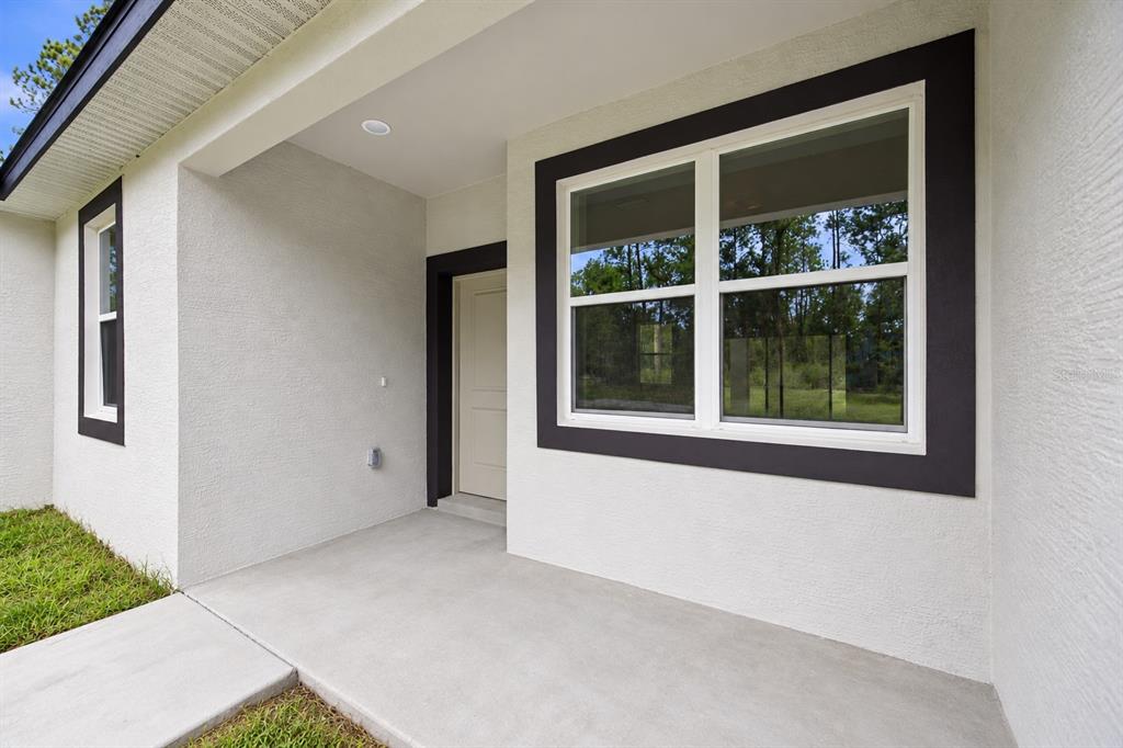A concrete porch leads to a beige door and a window with dark trim — 3839 W MIDWAY DRIVE, CITRUS SPRINGS, FL