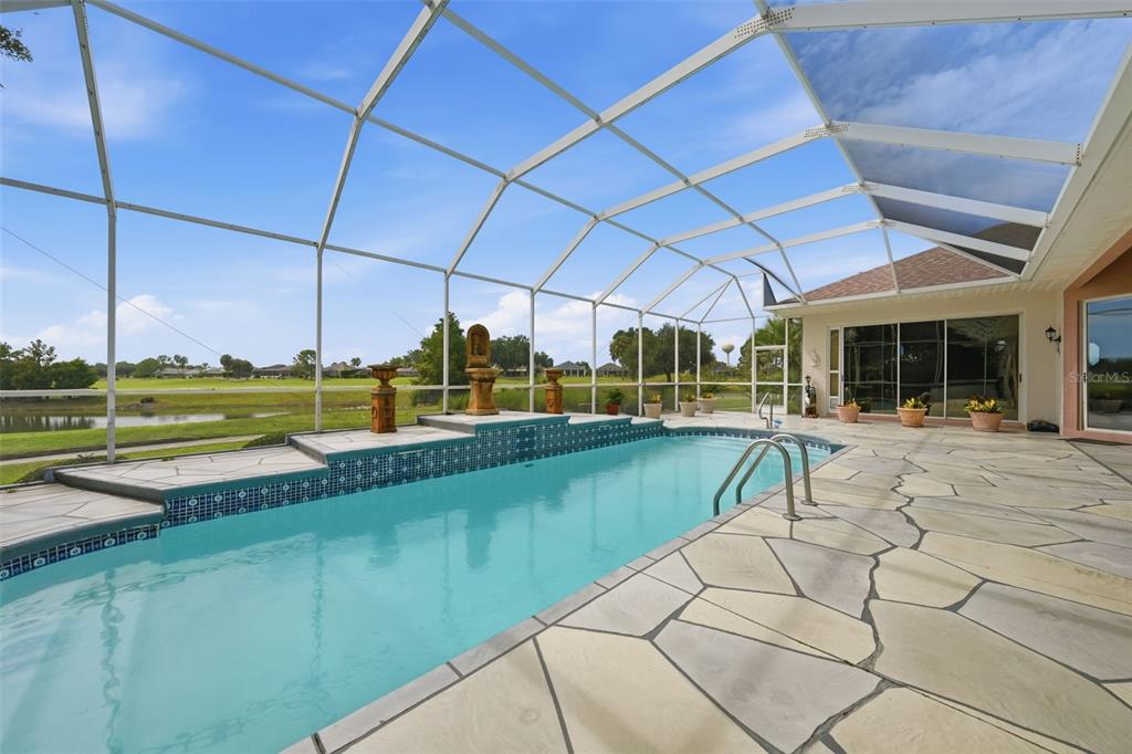 A screened-in swimming pool with a stone deck overlooks a pond and golf course — 1722 ENRIQUE DRIVE, THE VILLAGES, FL