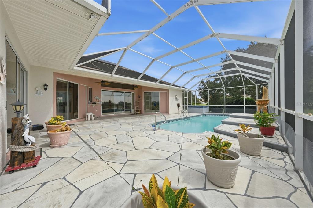 A screened-in pool patio features a stone-patterned deck, potted plants, and a swimming pool — 1722 ENRIQUE DRIVE, THE VILLAGES, FL