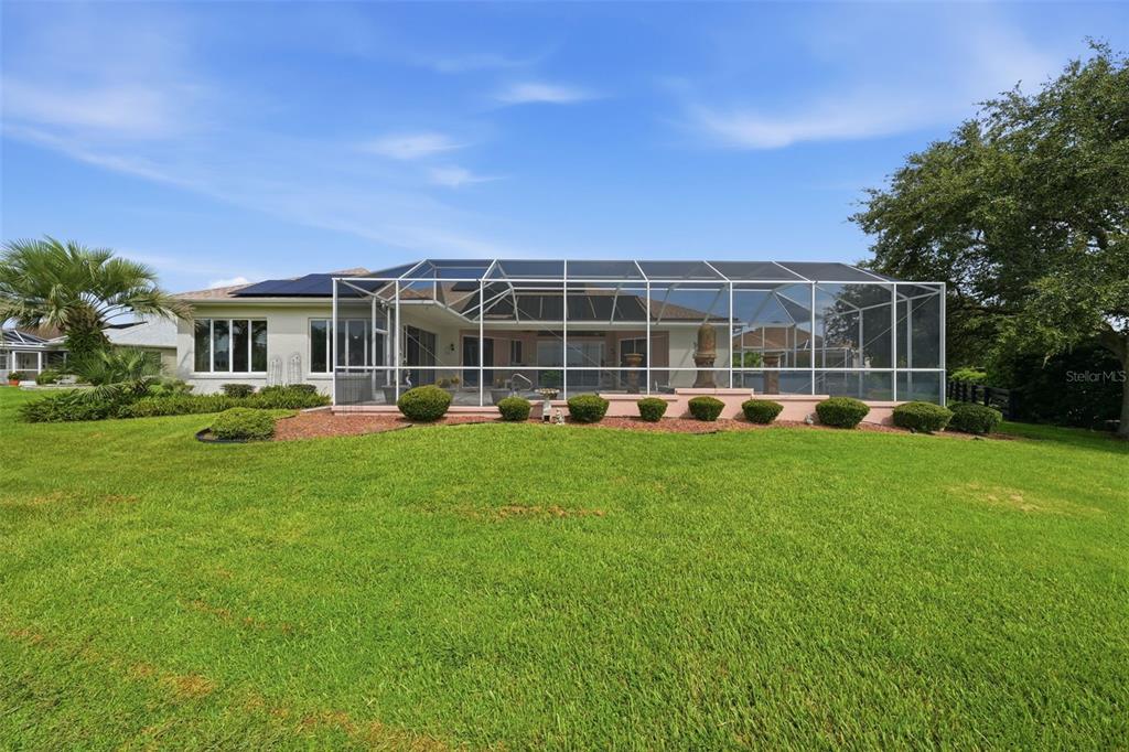 A house with a screened-in pool enclosure sits on a large, grassy backyard lawn — 1722 ENRIQUE DRIVE, THE VILLAGES, FL