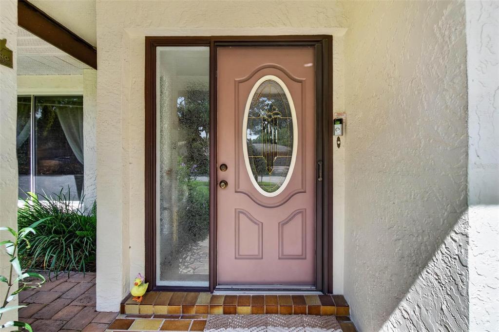 A pink front door with an oval glass insert sits beside a sidelight on a porch — 5674 BAY PINES LAKES BOULEVARD, ST PETERSBURG, FL