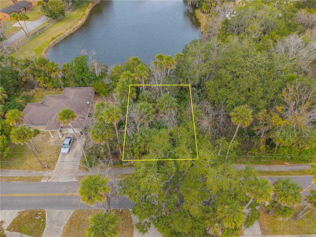 An aerial view shows a vacant, tree-covered residential lot outlined in yellow next to a house — ENTERPRISE AVENUE, NEW SMYRNA BEACH, FL