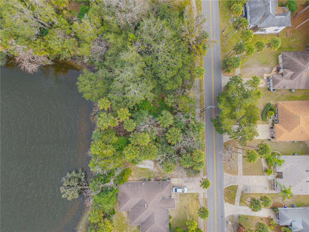 An aerial view shows a wooded lot situated between a lake and a residential street — ENTERPRISE AVENUE, NEW SMYRNA BEACH, FL