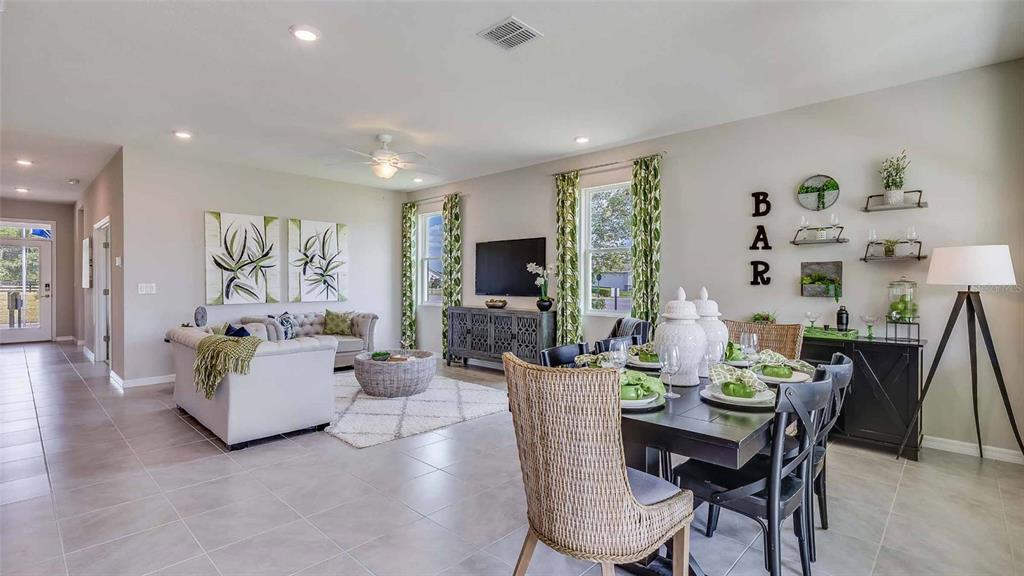 An open-concept living and dining room features tile floors, a neutral palette, and green curtains — 17290 SALTBUSH TRAIL, PARRISH, FL