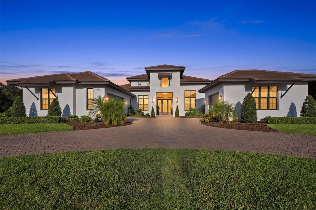 A modern single-story house with a paved driveway, tiled roof, and symmetrical exterior lighting — 1422 OAK MEADOW POINT, NEW PORT RICHEY, FL