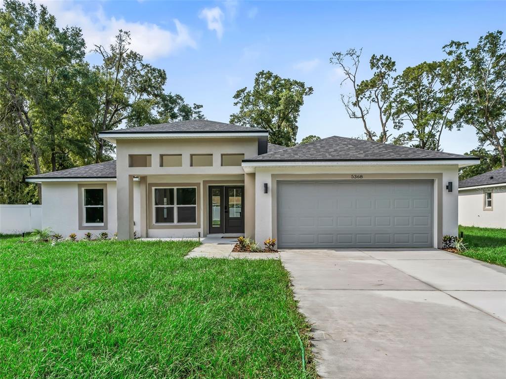 A single-story house with a gray garage door, stucco exterior, and a concrete driveway — 5386 NW 54TH PLACE, OCALA, FL