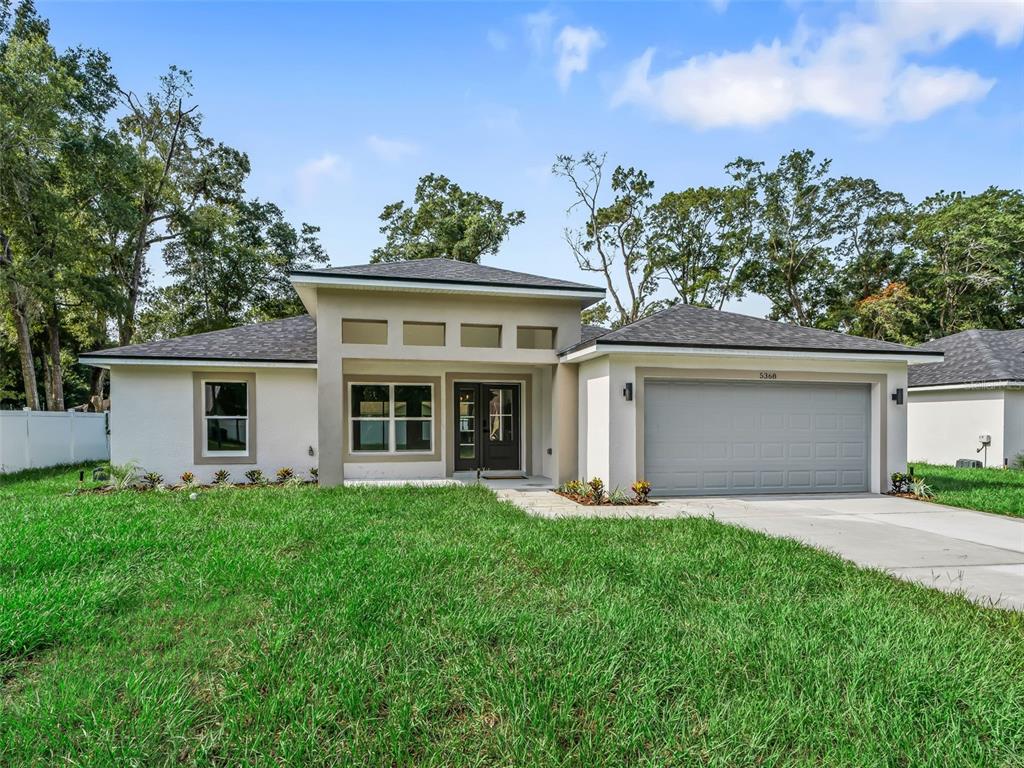 A single-story house with a gray garage, white stucco exterior, and a dark shingled roof — 5386 NW 54TH PLACE, OCALA, FL