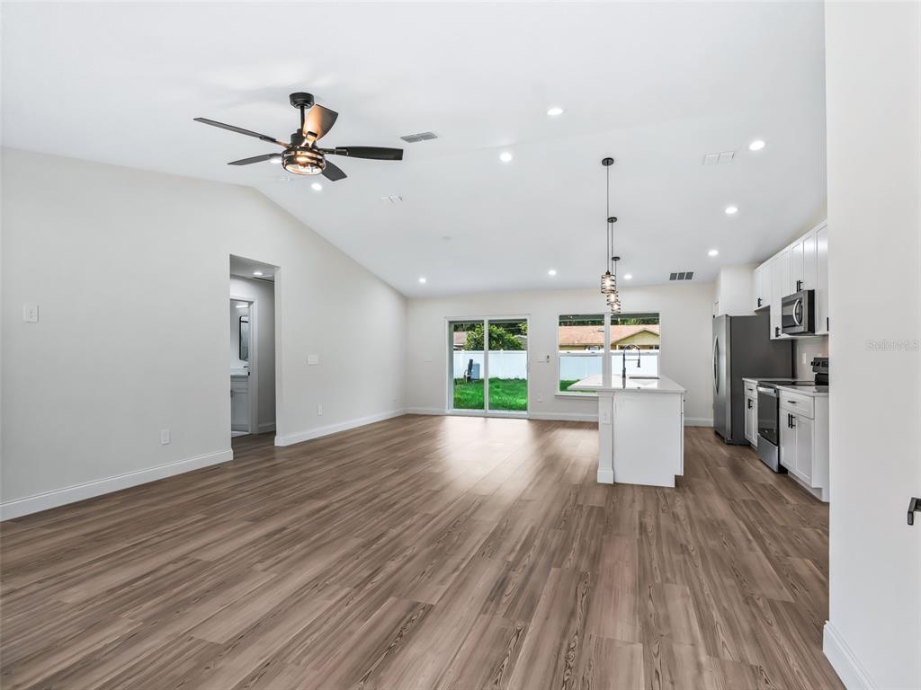 An open-concept living area features wood-look flooring, a vaulted ceiling, and a modern white kitchen — 5386 NW 54TH PLACE, OCALA, FL