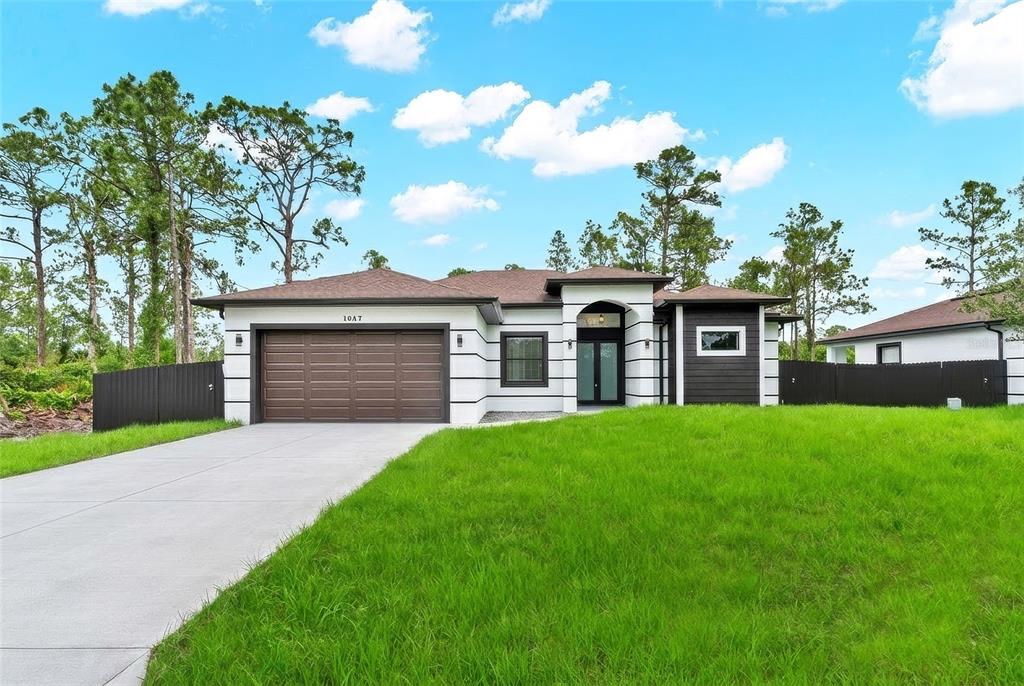A modern single-story house with a two-car garage, white and dark siding, and a lawn — 1047 MERRY STREET E, LEHIGH ACRES, FL