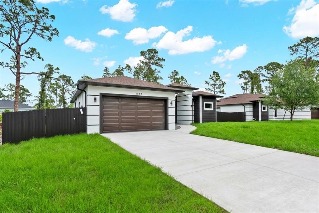A modern single-story house with a white and dark brown exterior and a concrete driveway — 1047 MERRY STREET E, LEHIGH ACRES, FL