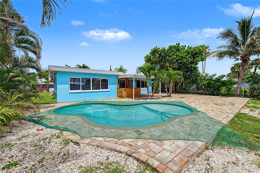 A light blue house with a pool covered by a green safety net in the backyard — 403 NORMANDY ROAD, MADEIRA BEACH, FL