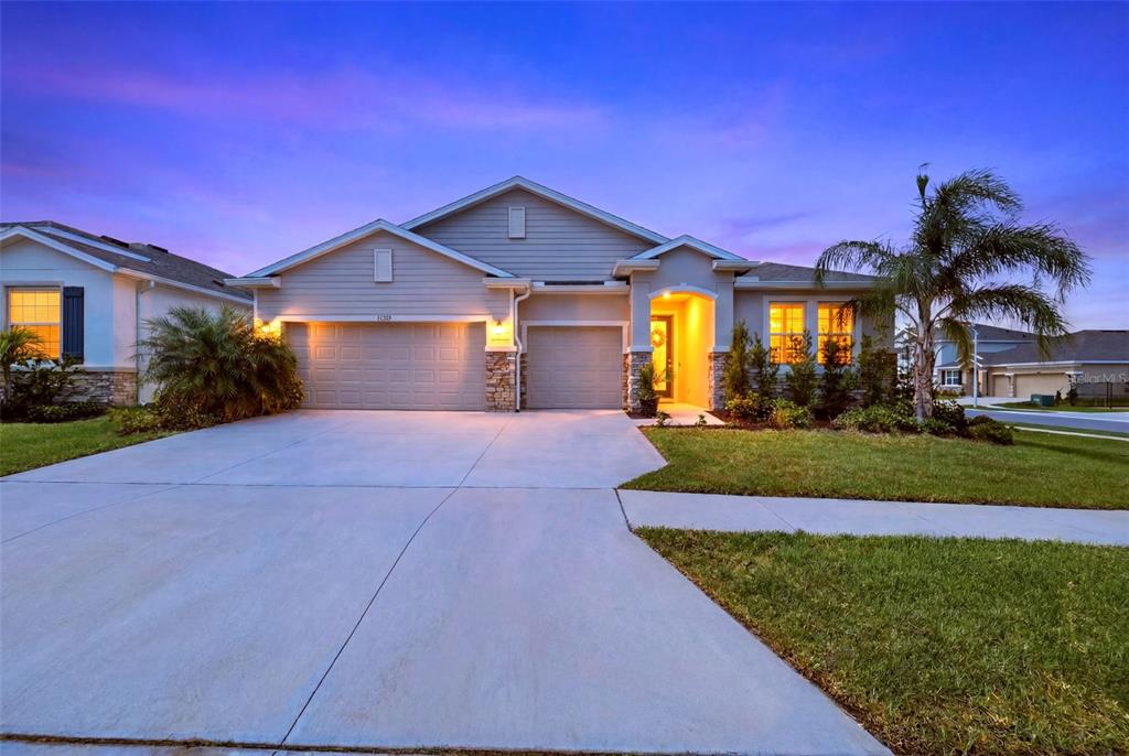 A single-story suburban house features a tan exterior, stone accents, and a three-car garage — 32337 CONCHSHELL SAIL STREET, WESLEY CHAPEL, FL