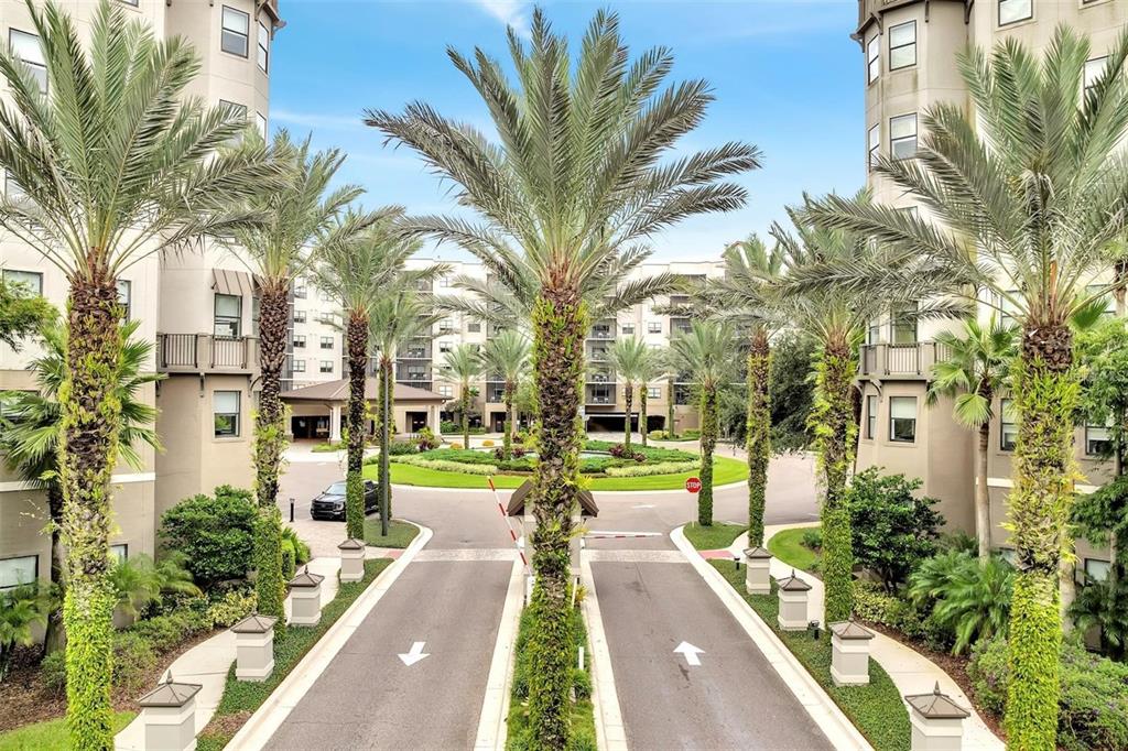 An exterior view of a gated apartment complex entrance with palm trees and a circular driveway — 14501 GROVE RESORT AVENUE UNIT 2221, WINTER GARDEN, FL