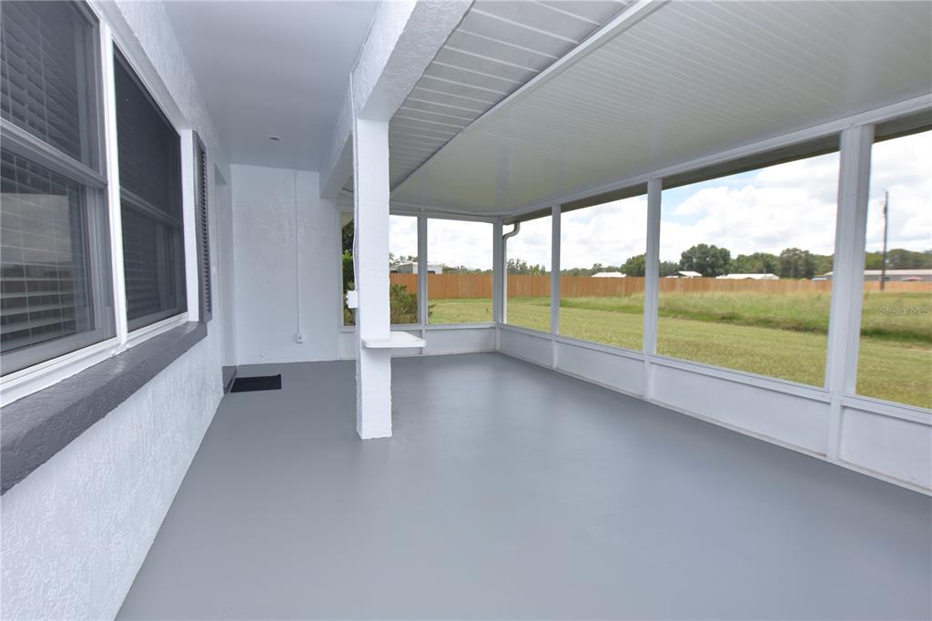 A covered patio with gray flooring, white support columns, and screened walls overlooking a grassy yard — 3602 BRUTON ROAD, PLANT CITY, FL