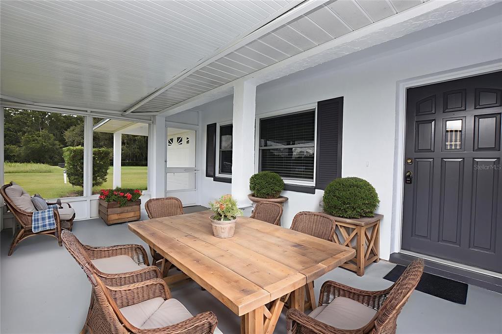 A covered patio features a wooden dining table, wicker chairs, and a dark front door — 3602 BRUTON ROAD, PLANT CITY, FL