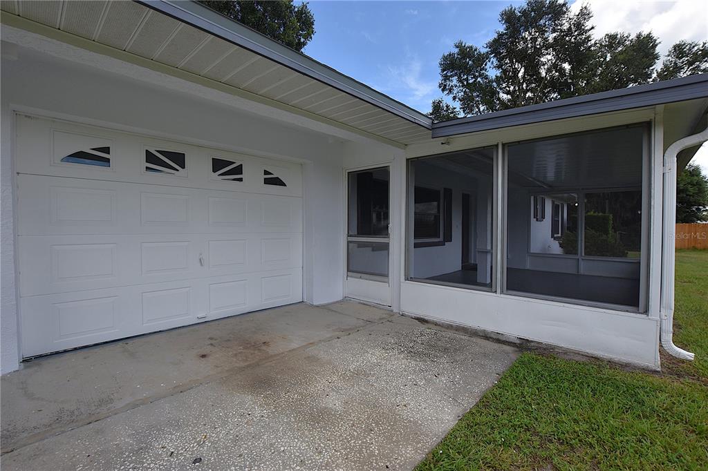 A white garage door sits beside a screened-in porch with a concrete driveway in front — 3602 BRUTON ROAD, PLANT CITY, FL