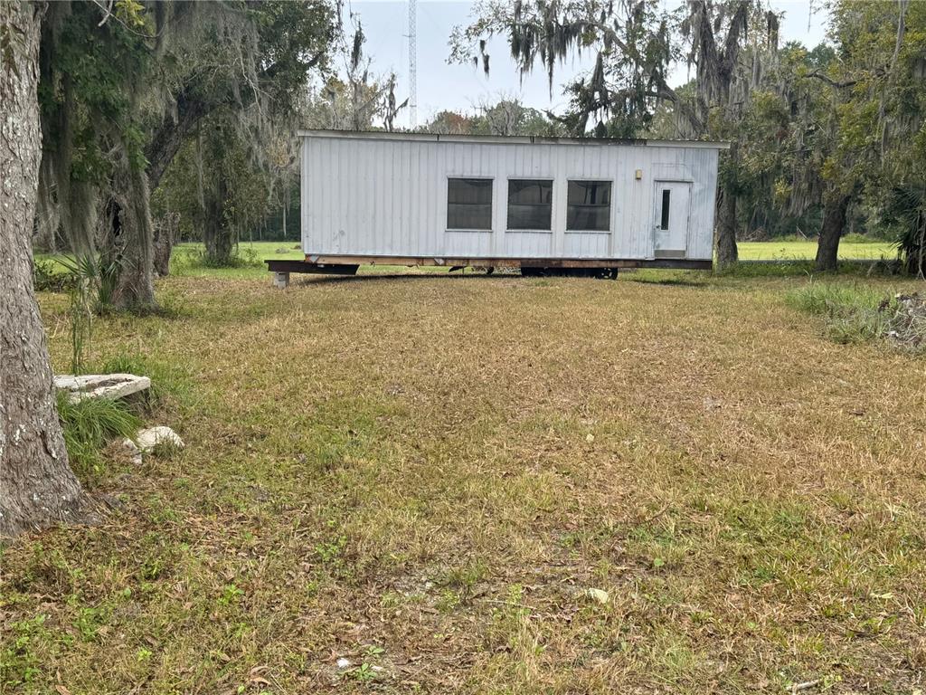 A white, rectangular mobile home sits on a grassy lot surrounded by mossy trees — 108 E MARKET ROAD, STARKE, FL