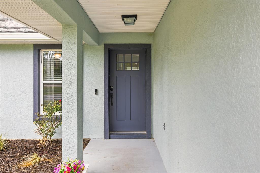 A front porch features a dark gray door, light green stucco walls, and a window — 47 REDWOOD TRACK COURSE, OCALA, FL