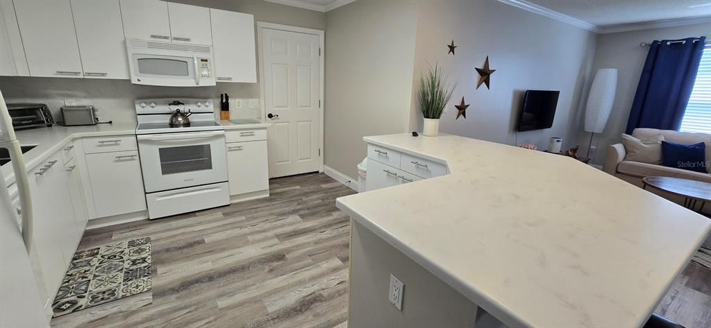 A kitchen with white cabinets, light countertops, and wood-look flooring opens to a living area — 712 ARTESIA AVENUE, THE VILLAGES, FL