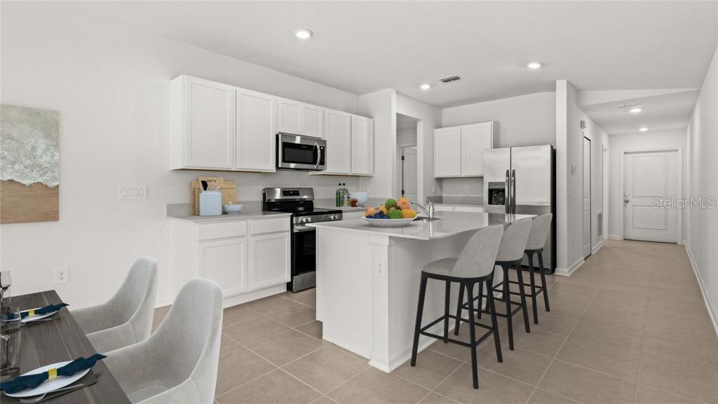 A modern kitchen features white cabinets, a central island with bar stools, and stainless appliances — 1580 WILLOW GARDEN LOOP, EUSTIS, FL