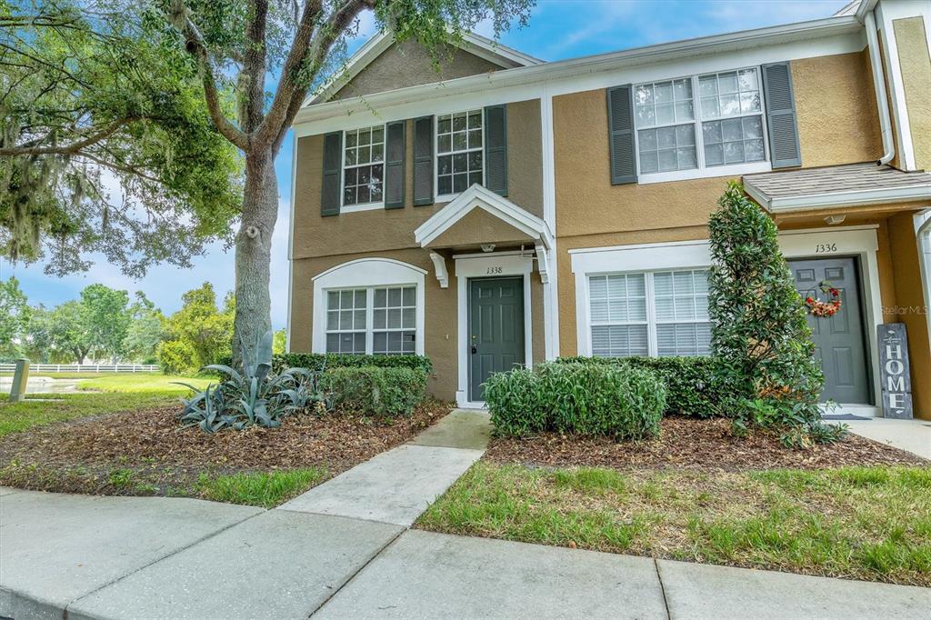 A two-story townhouse exterior features tan stucco walls, dark shutters, and two front entry doors — 1338 STANDRIDGE DRIVE, ZEPHYRHILLS, FL